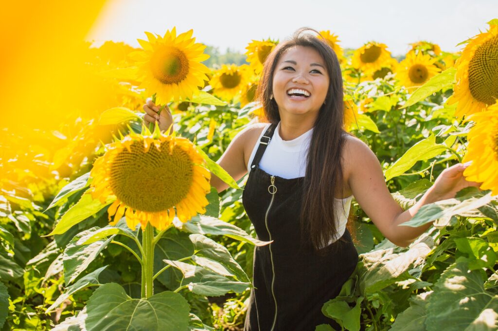 A woman smiles in field of sunflowers, feeling her best after visiting Heal n Cure, a wellness center in Glenview.