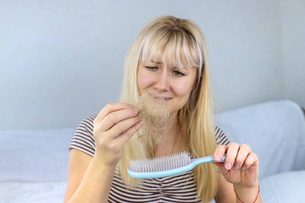 A woman pulls a clump of hair from her comb with a distressed look on her face. This is an example of a common concern that makes patients seek our help for hair restoration near Wilmette